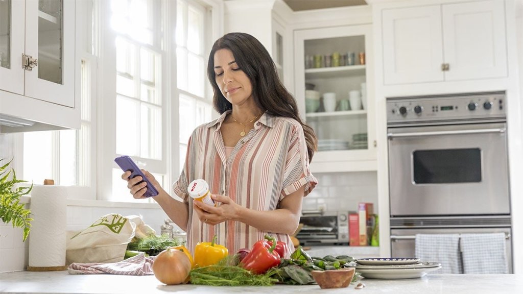Person using the CVS Health app on their phone to check prescription details while standing in a bright kitchen with fresh produce on the counter