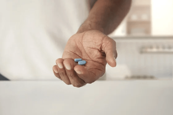 A close-up of a person holding two blue pills in their hand (Journavx (suzetrigine)) with a neutral background.