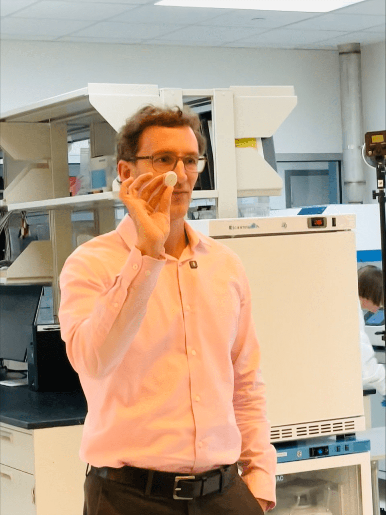 A researcher holding a small, round wearable health monitoring device in a laboratory setting.