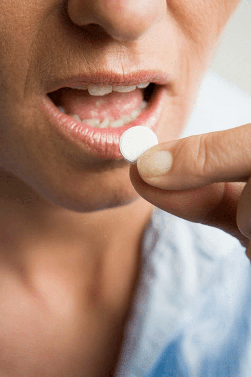 A close-up image of a person preparing to take a white pill, with their mouth slightly open.