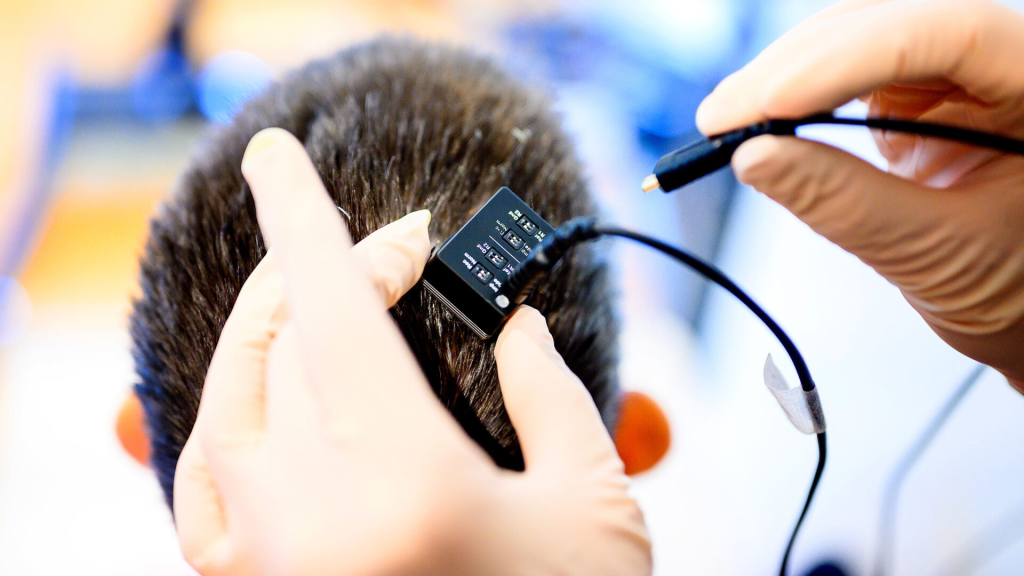 A researcher attaching a brain-computer interface device with electrodes to the back of a person's head for a neuroprosthesis study.