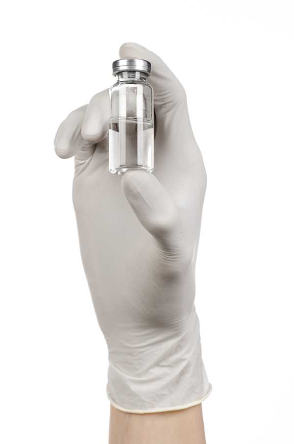 A gloved hand holding a small glass vial containing a clear liquid.