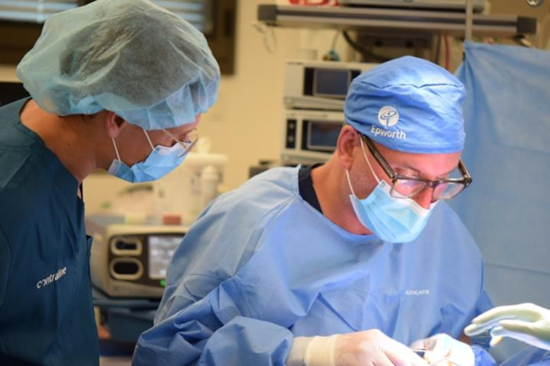 Surgeons performing a medical procedure in an operating room, wearing scrubs and masks for safety.