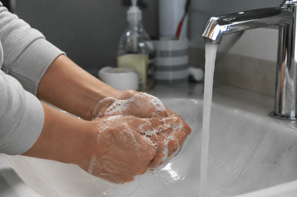 Person washing their hands with soap under running water at a kitchen sink.