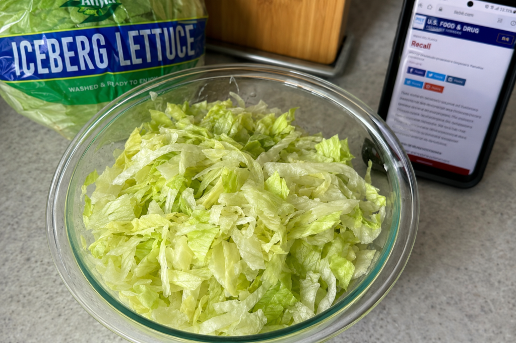 Bowl of chopped iceberg lettuce beside a packaged head of lettuce and a smartphone displaying food safety information.