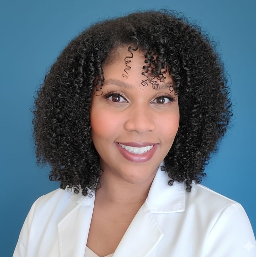A smiling woman with curly hair wearing a white lab coat against a blue background.