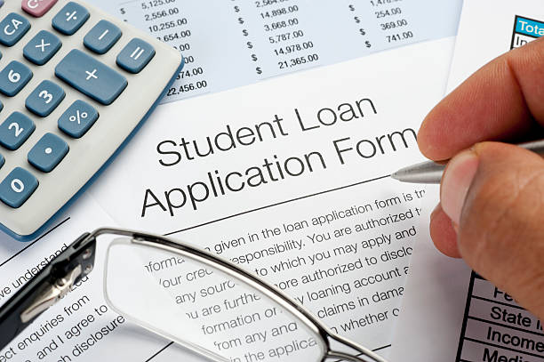 Close-up of a student loan application form with a calculator and hand holding a pen.