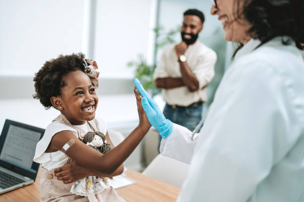 Child smiling and high-fiving a healthcare professional during a pediatric visit, with family in the background.