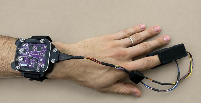 Person wearing the EquiVitals/ChromaSense pulse oximeter prototype on their wrist and finger.